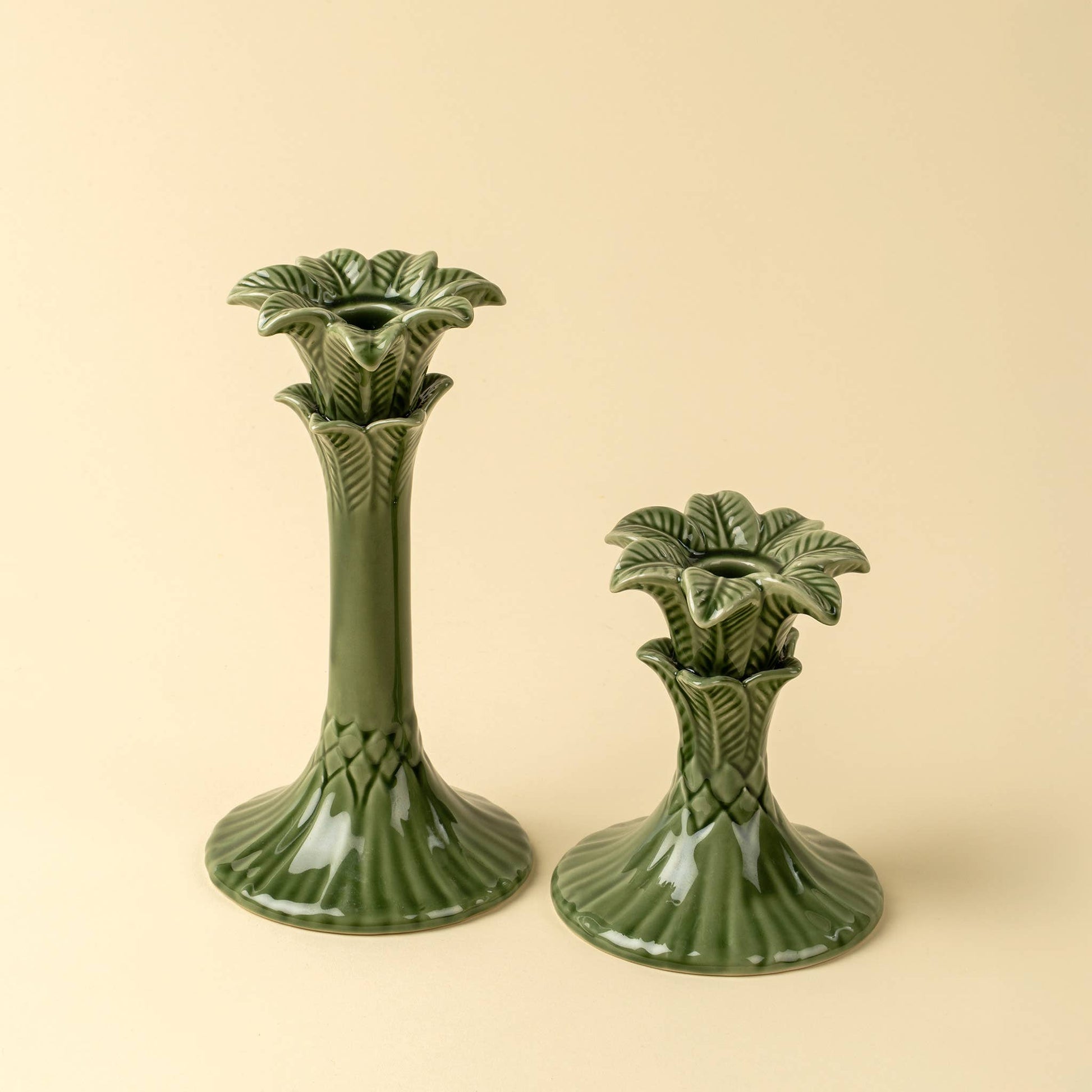Two green ceramic candle holders with leaf design on a beige background
