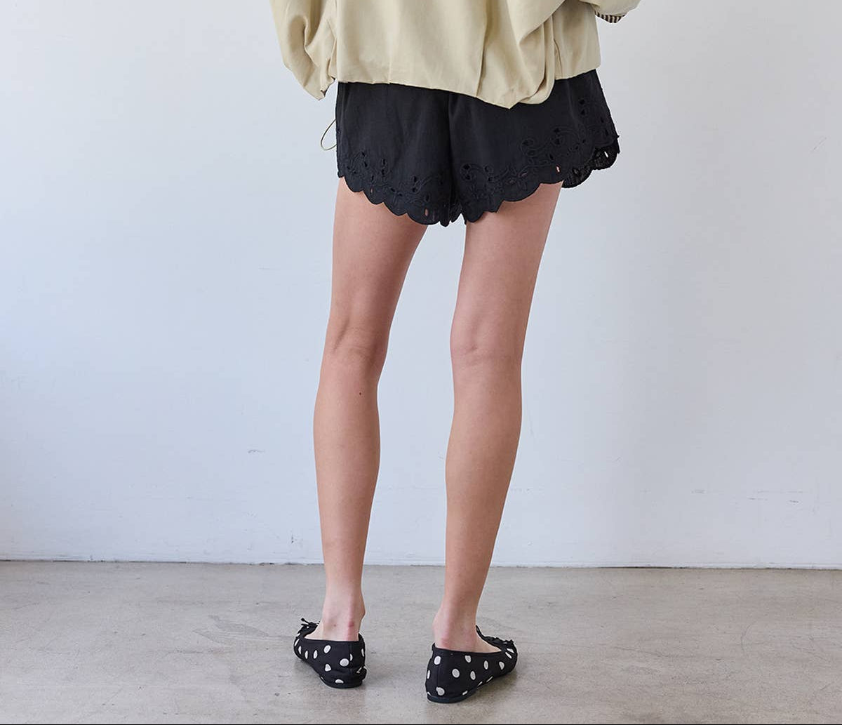 Person wearing a beige jacket and black shorts against a white background