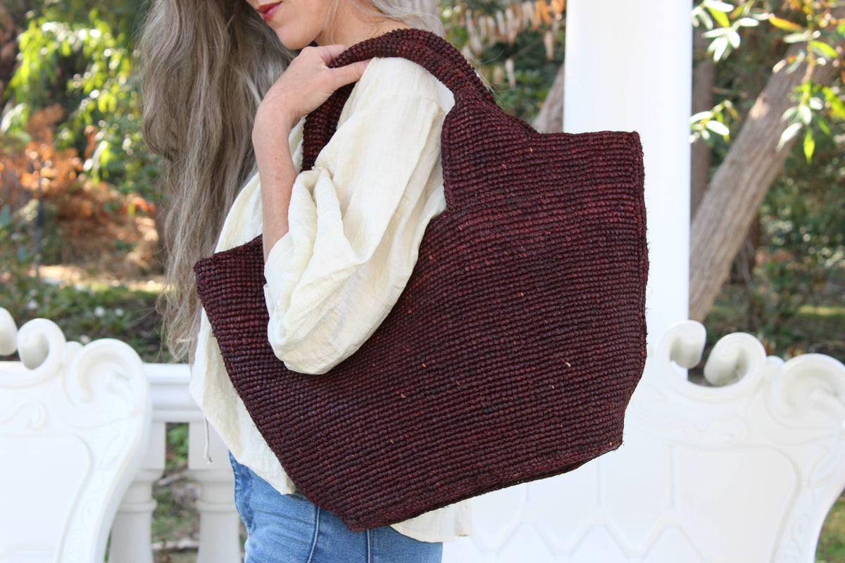 Person holding a brown woven tote bag outdoors