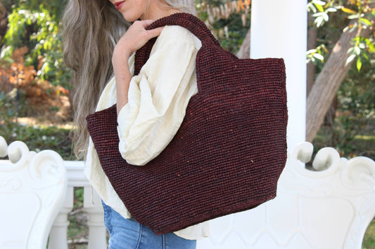 Person holding a brown woven tote bag outdoors
