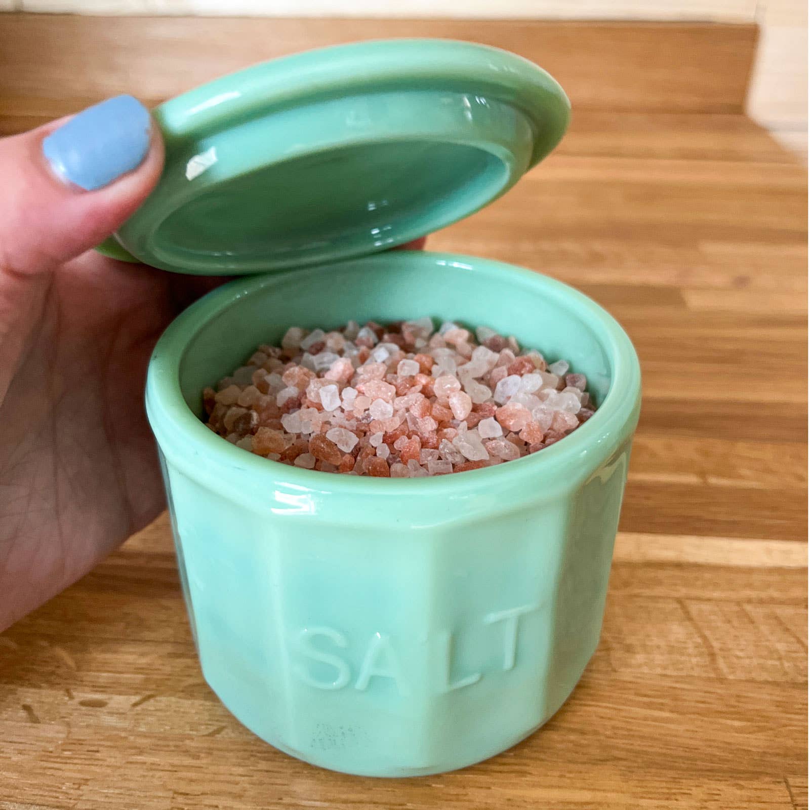 Light blue container of salt held by a hand on a wooden surface