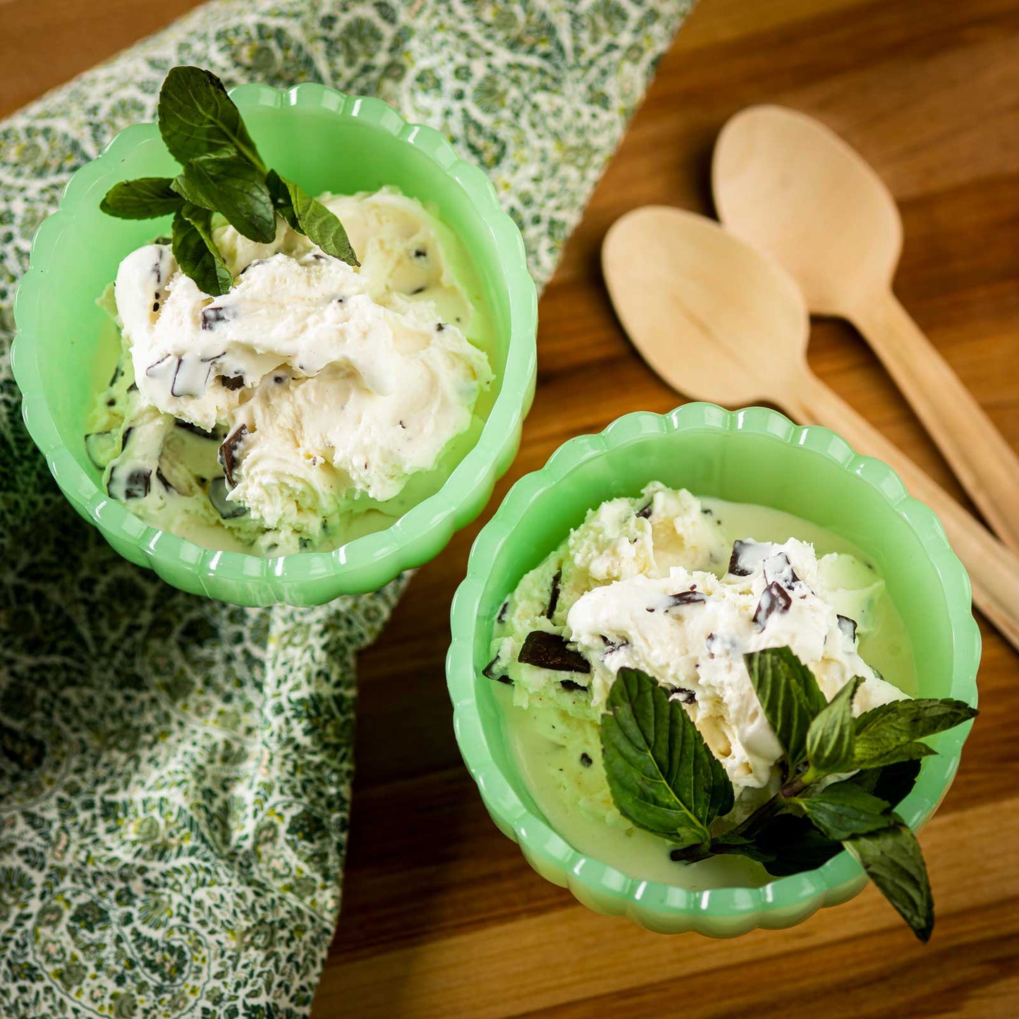Two green bowls of ice cream with mint leaves on a wooden surface.