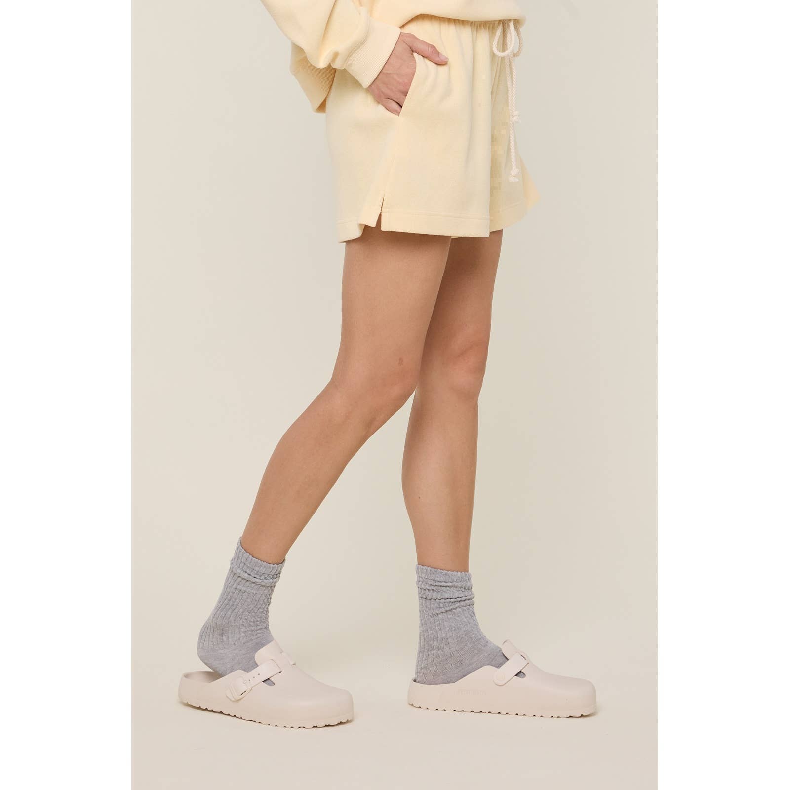 Person wearing light yellow outfit with gray socks and white shoes on a neutral background