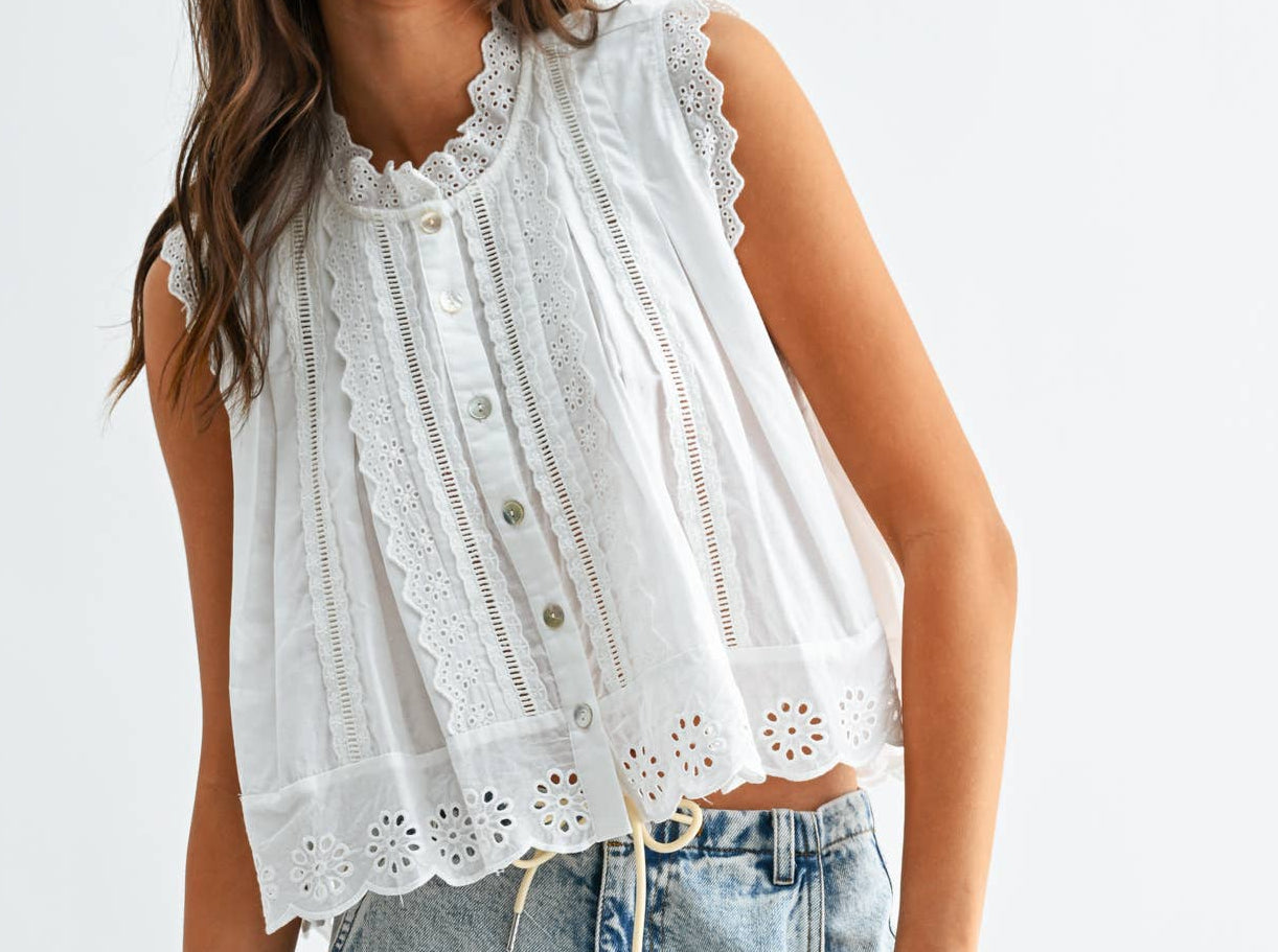 Woman wearing a white sleeveless top with lace details and light blue jeans on a white background