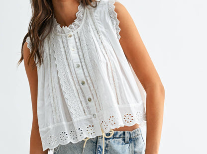 Woman wearing a white sleeveless top with lace details and light blue jeans on a white background