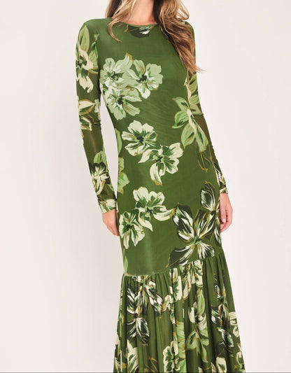 A woman modeling a long-sleeve maxi dress with a green and white floral print against a plain light background.