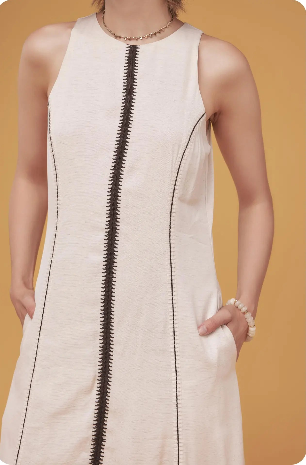 White sleeveless dress with a black zipper on a mustard yellow background