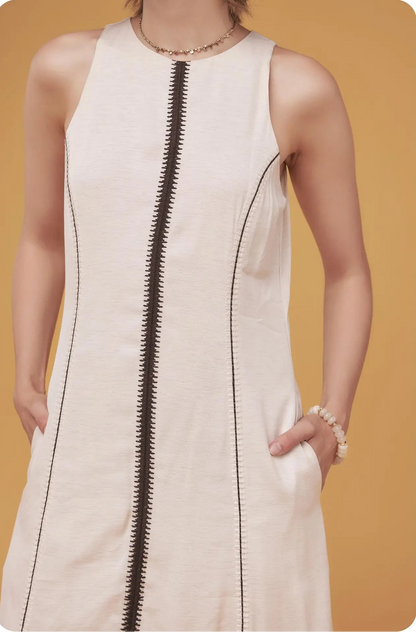White sleeveless dress with a black zipper on a mustard yellow background