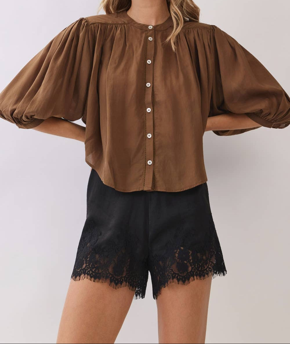 Woman wearing a brown blouse with puffed sleeves and black lace shorts on a white background