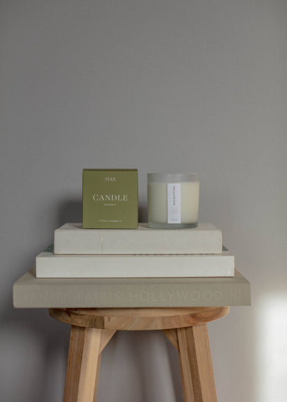 Candle and box on stacked books with a wooden stool against a gray wall