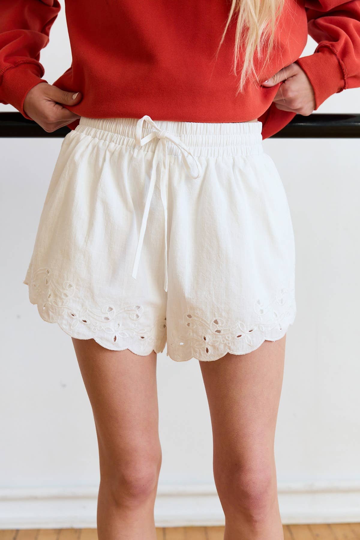 Person wearing a red sweater and white eyelet shorts against a plain background
