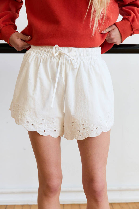 Person wearing a red sweater and white eyelet shorts against a plain background