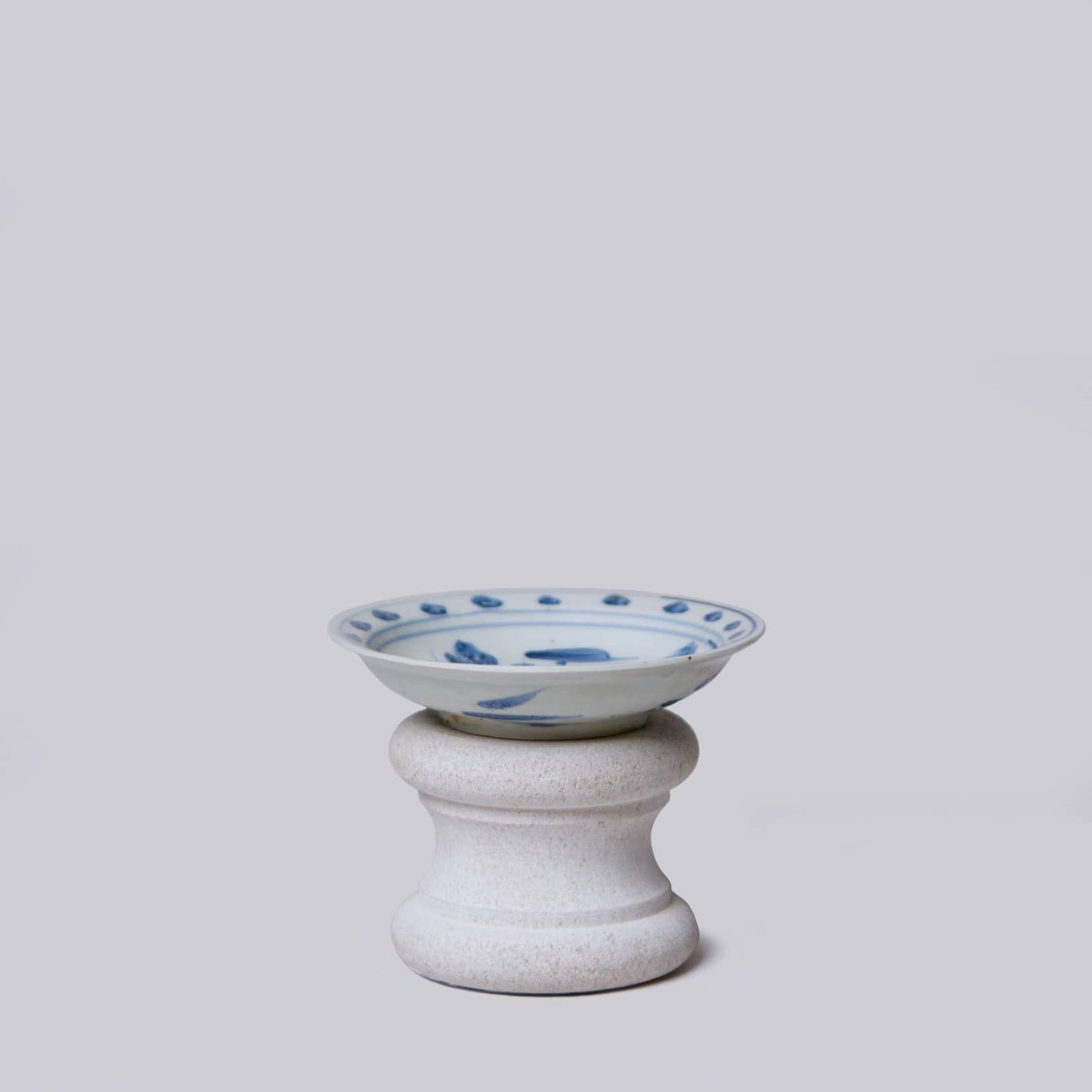 Ceramic bowl with blue patterns on a white pedestal against a light gray background