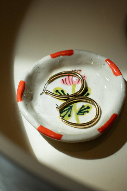 Ceramic dish with decorative elements and a pair of earrings on a neutral background