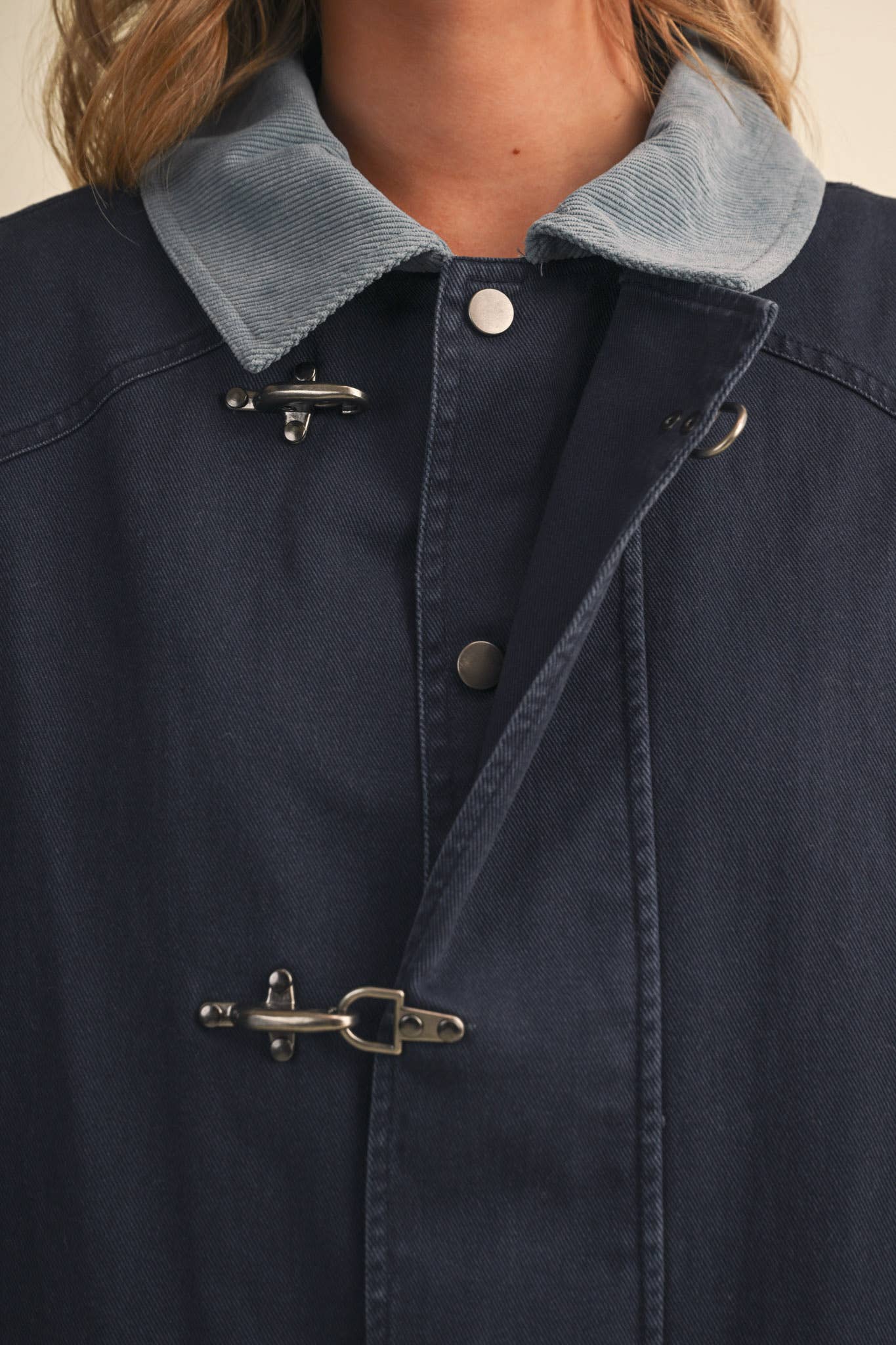 Close-up of a navy blue coat with a light blue corduroy collar and silver toggle closures, worn by a model.