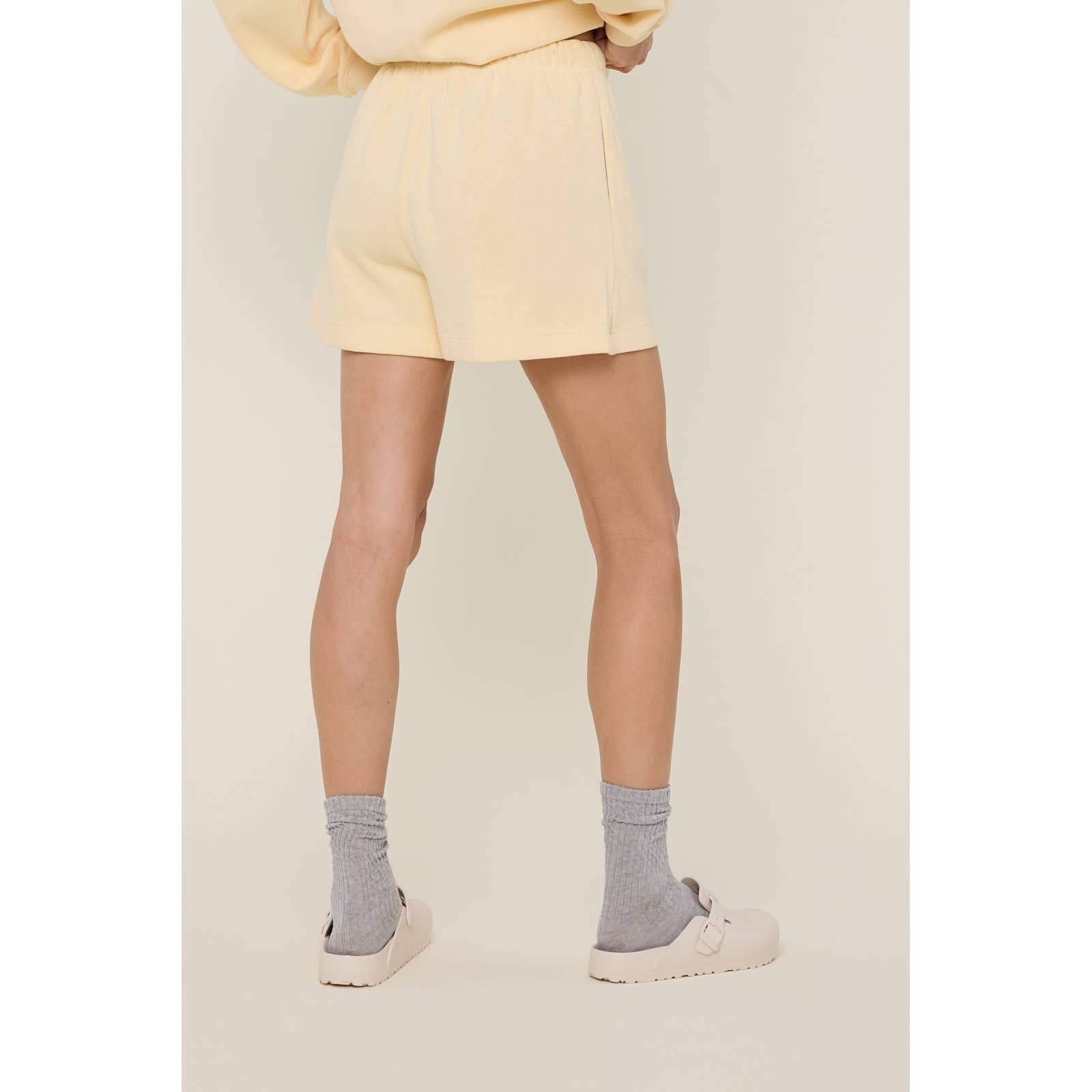 Person wearing a light yellow outfit with shorts and a matching top, standing against a plain background.