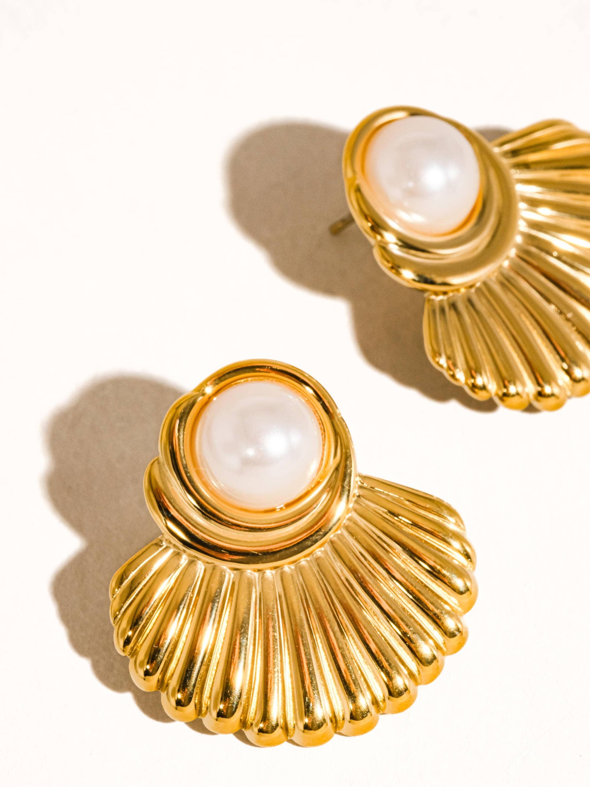 Gold earrings with pearl-like centers on a beige background