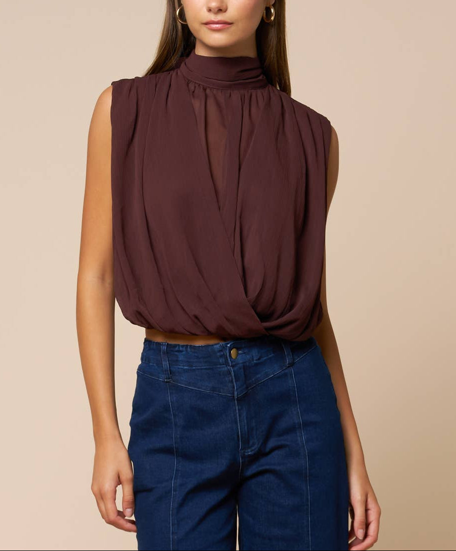 Woman wearing a brown sleeveless top and blue jeans against a beige background