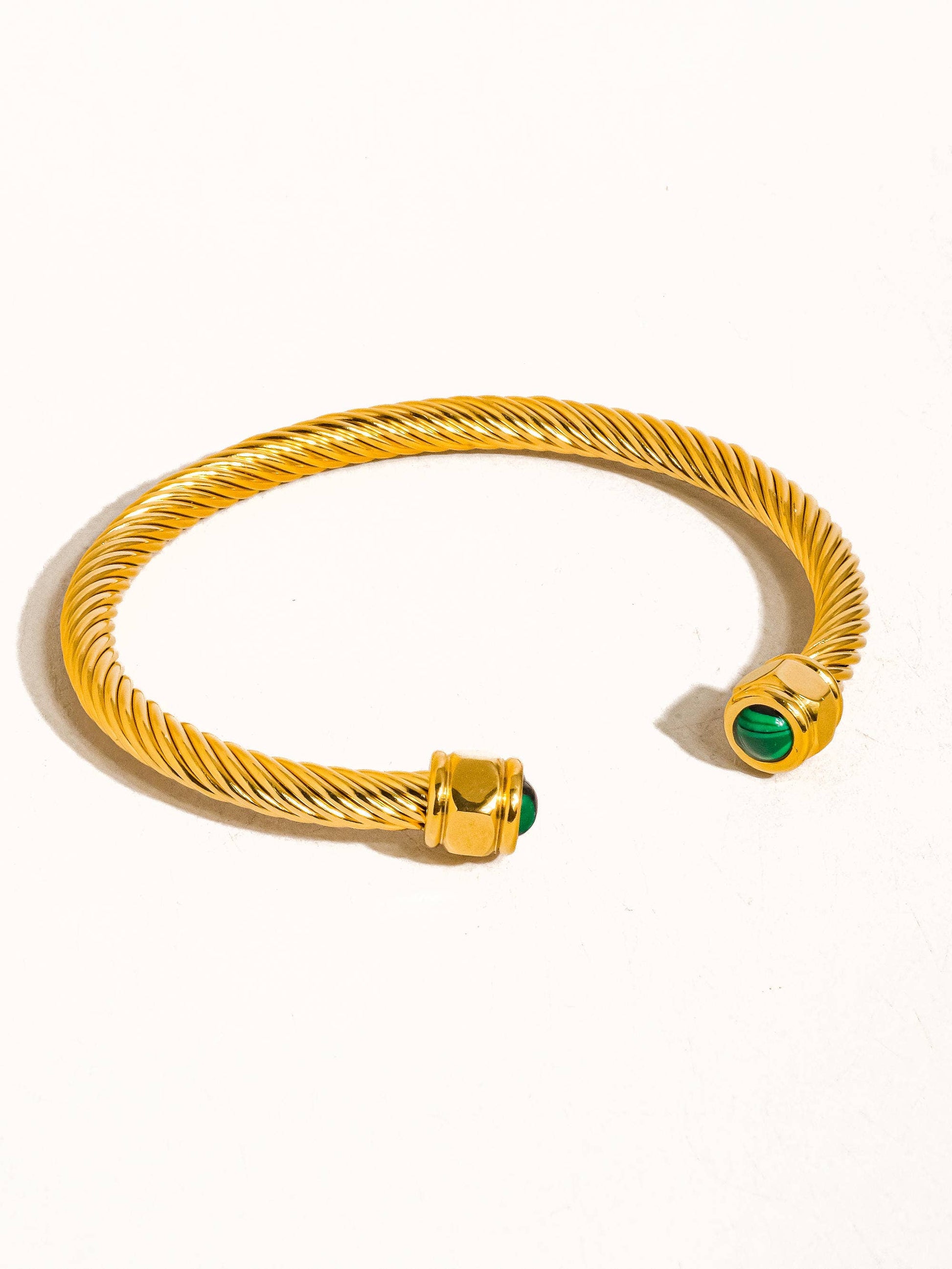 Gold bracelet with green gemstones on a white background