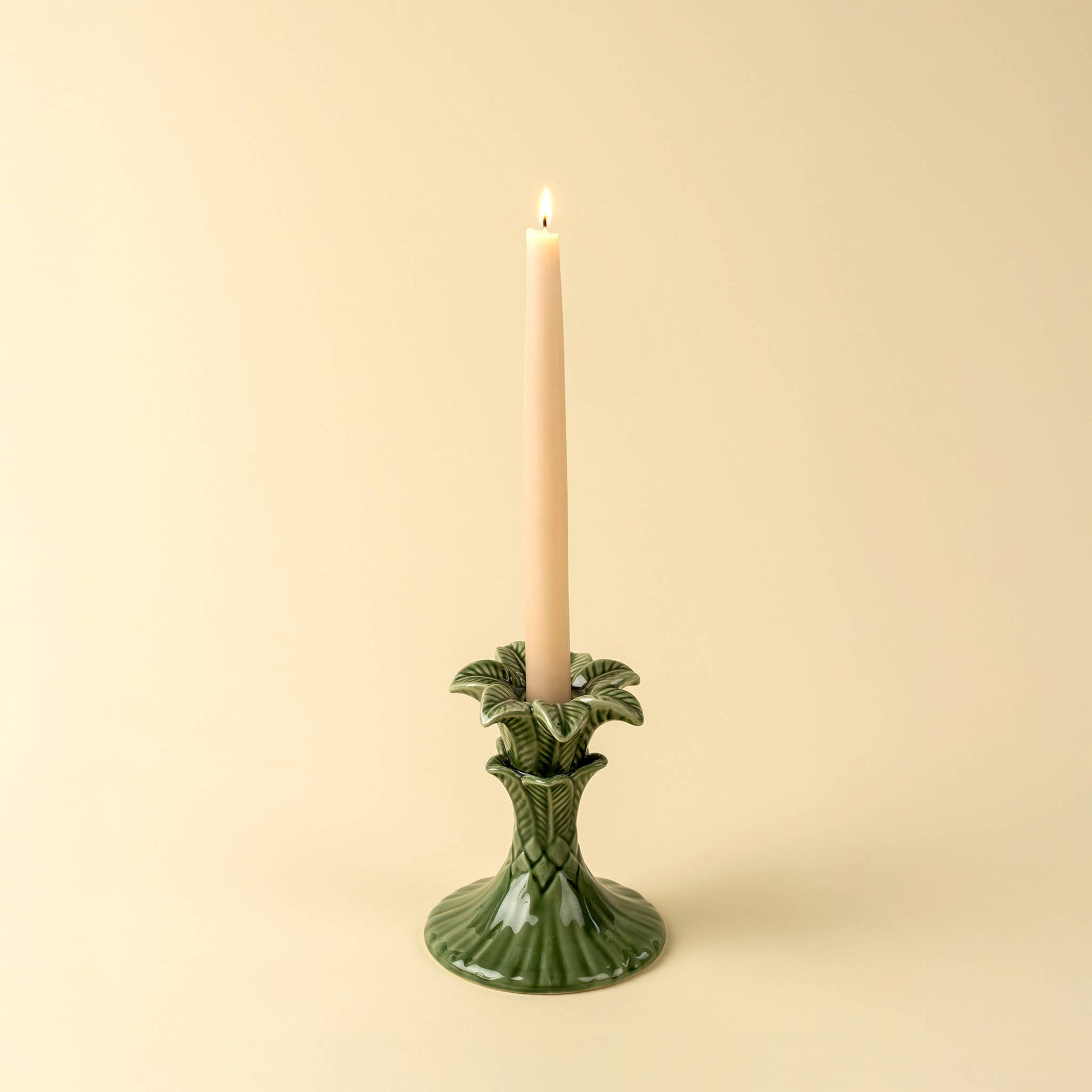 Green candle holder with a lit candle on a beige background