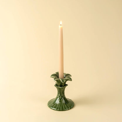 Green candle holder with a lit candle on a beige background