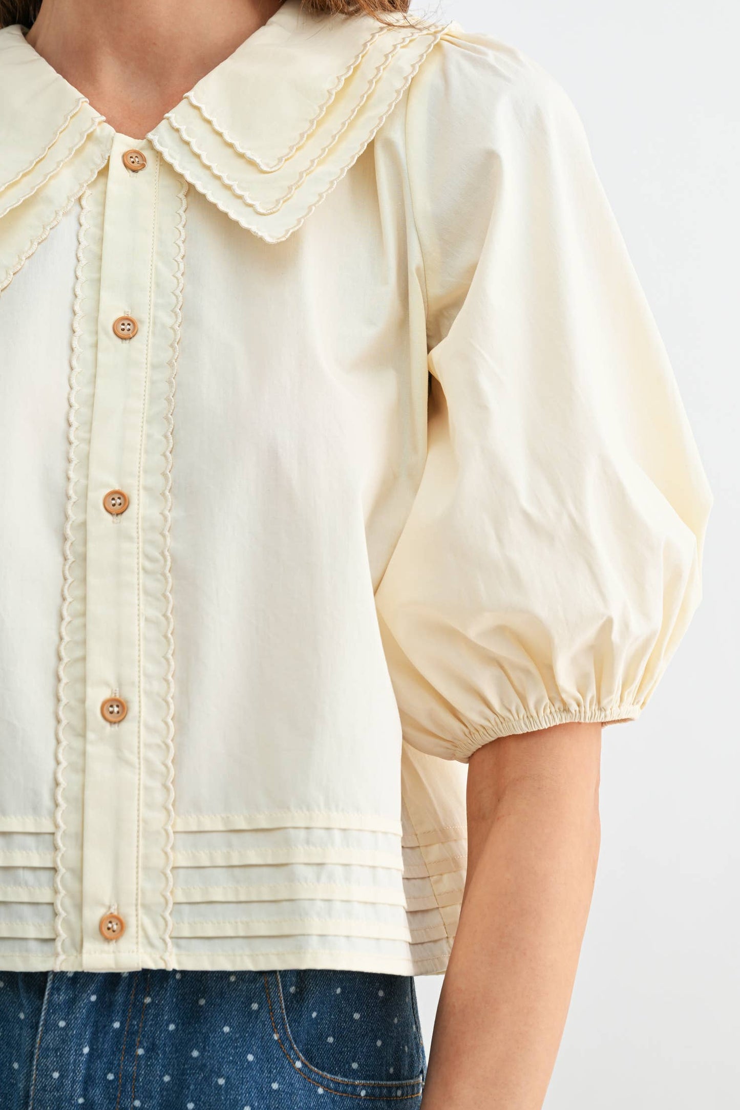 Woman wearing a cream-colored blouse with lace collar and buttons on a white background