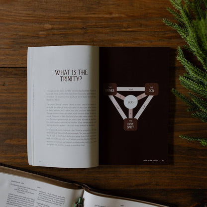 Open book on a wooden surface with a diagram of the Trinity on a dark background