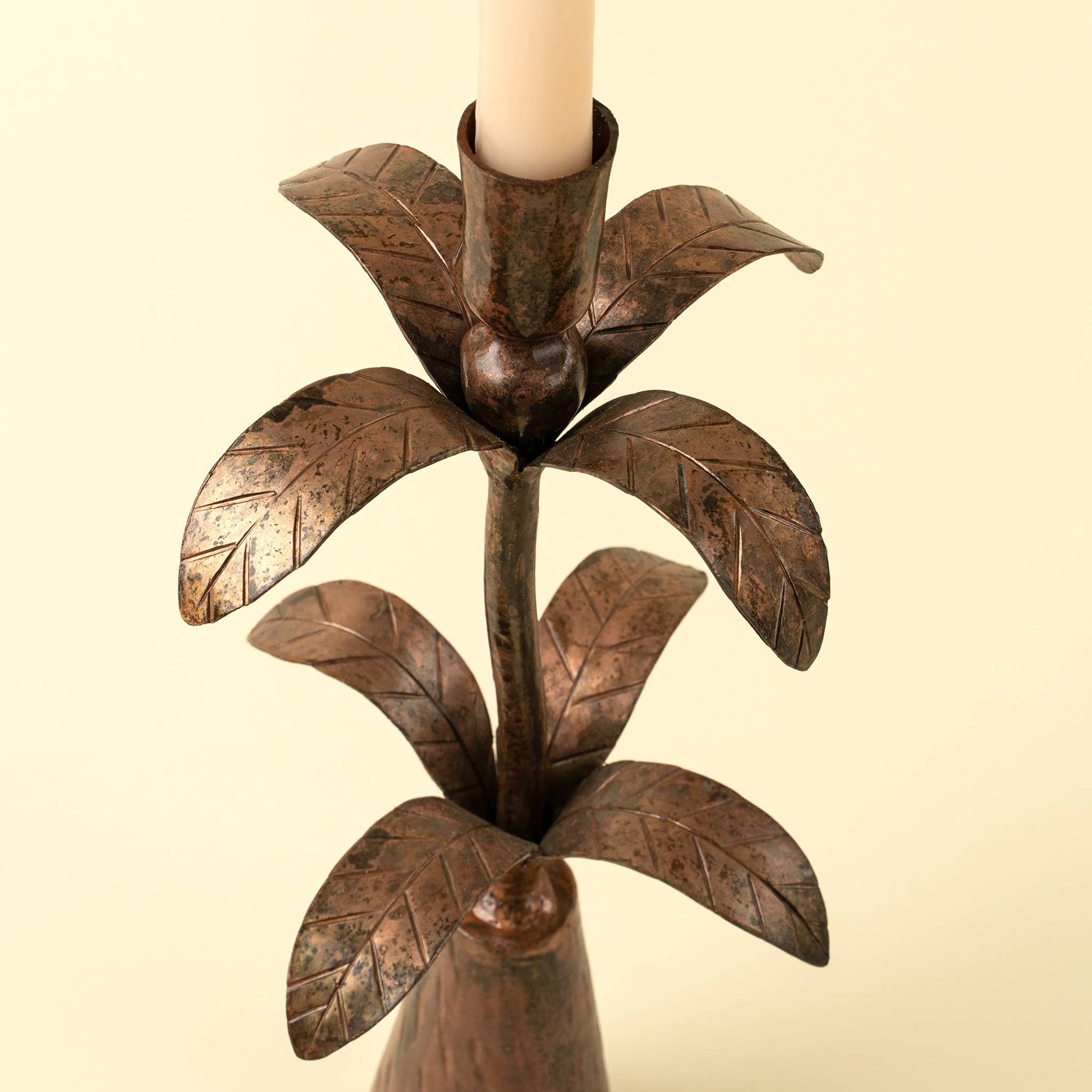 Bronze leaf-shaped candle holder with a candle on a beige background