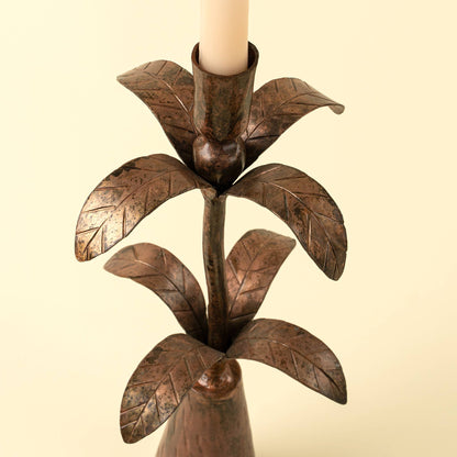 Bronze leaf-shaped candle holder with a candle on a beige background