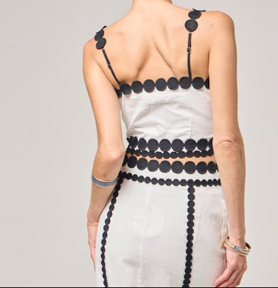 Woman wearing a white dress with black embellishments on a plain background