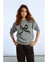 Woman wearing a gray sweater with a black bow design on a light gray background