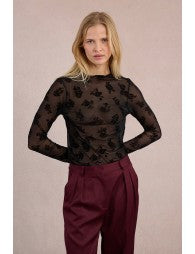 Woman wearing a black patterned top and burgundy pants against a beige background
