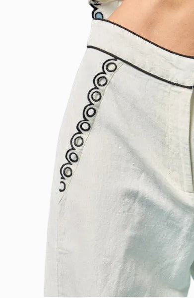 White pants with black decorative trim on a light blue background