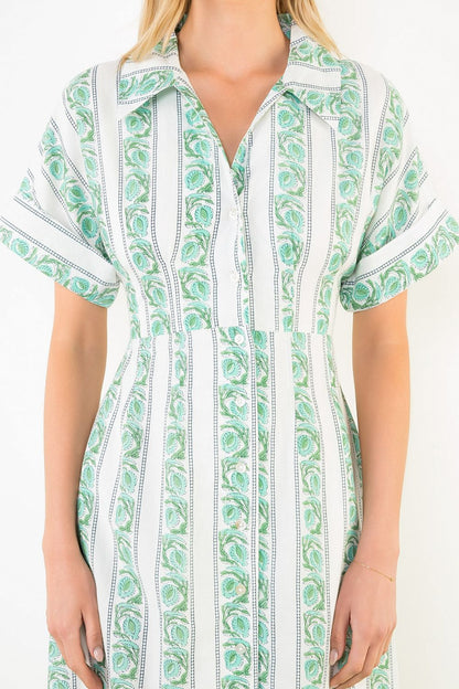 Green and white patterned dress worn by a person on a plain background