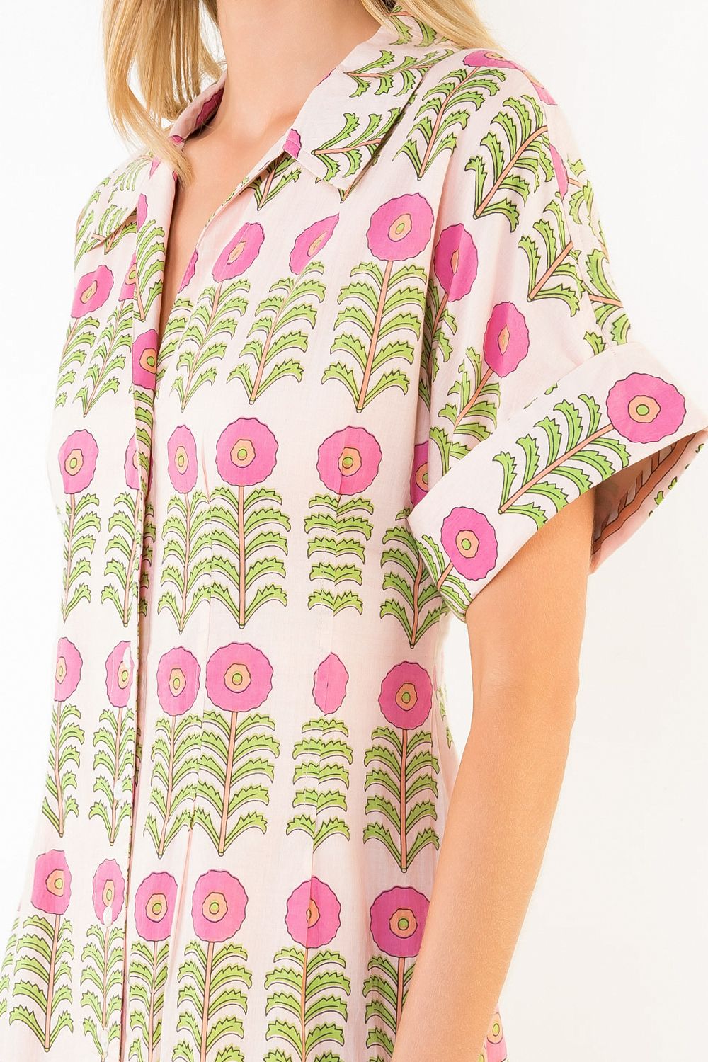 Woman wearing a floral patterned shirt with pink flowers and green leaves.