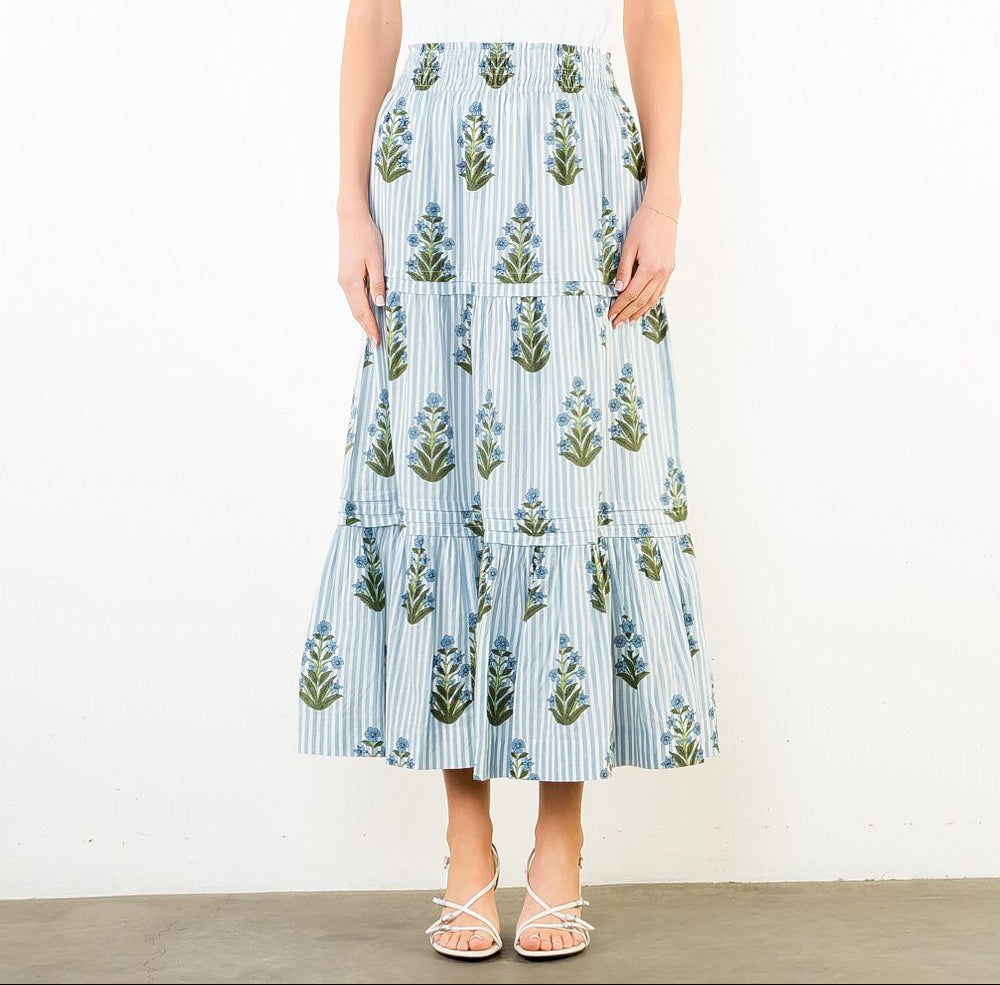 Woman wearing a white top and floral skirt on a plain background
