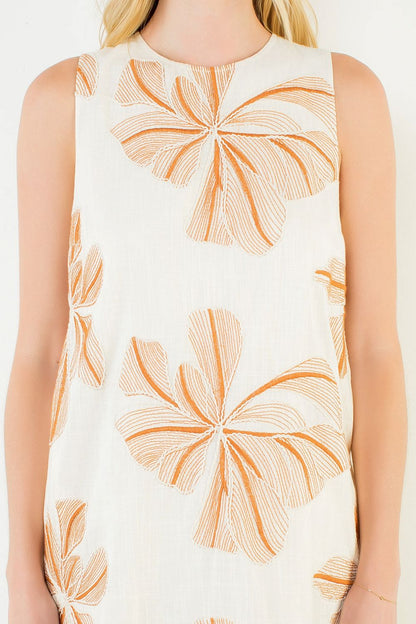 White sleeveless top with orange floral pattern worn by a person on a white background