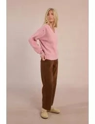 Person wearing a pink sweater and brown pants on a pink background